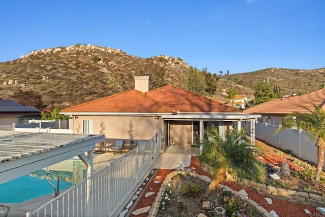 rear view of house with a fenced backyard, a chimney, a tile roof, a patio area, and a mountain view