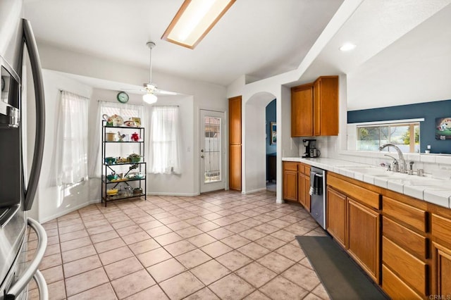 kitchen featuring arched walkways, brown cabinets, light tile patterned floors, stainless steel appliances, and a sink