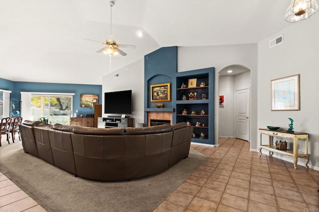 living area featuring arched walkways, ceiling fan, a fireplace, visible vents, and vaulted ceiling