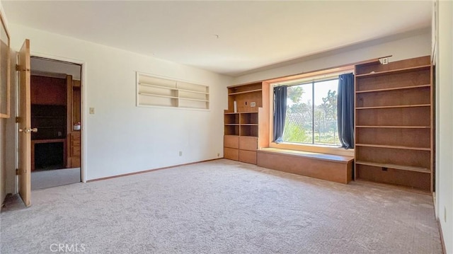 empty room with built in shelves, carpet, and baseboards