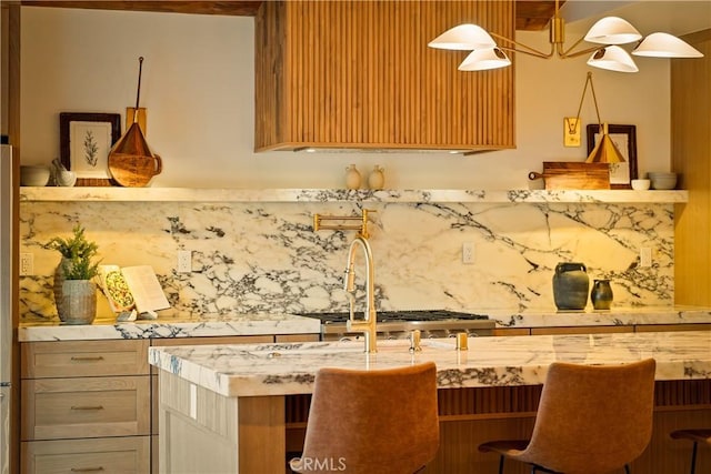 kitchen with a breakfast bar, light stone countertops, backsplash, and a sink