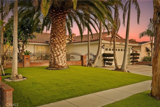 mediterranean / spanish house featuring fence, stucco siding, a lawn, driveway, and an attached garage