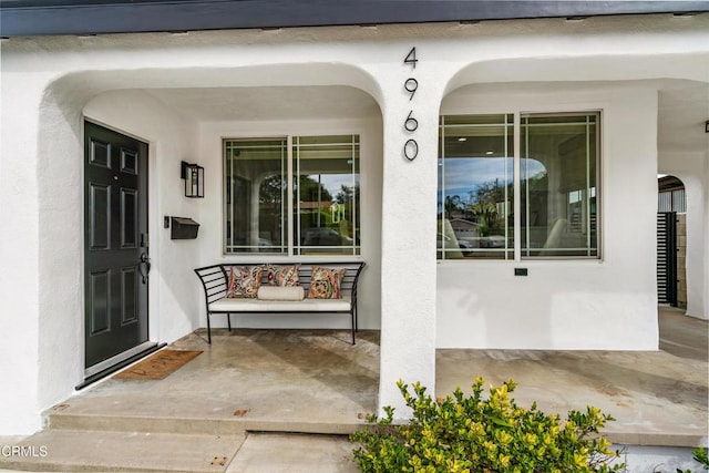 doorway to property with a porch and stucco siding