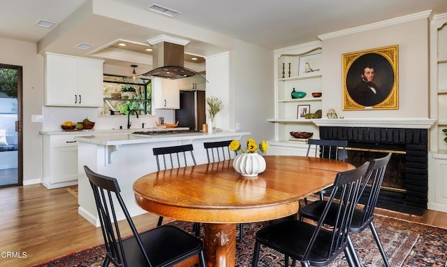 dining area with built in features, wood finished floors, visible vents, and crown molding