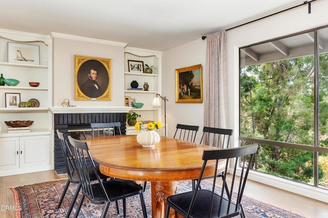 dining area featuring a brick fireplace, a healthy amount of sunlight, crown molding, and wood finished floors