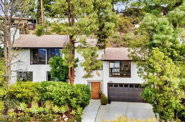 view of front of house featuring driveway, a shingled roof, a chimney, an attached garage, and stucco siding