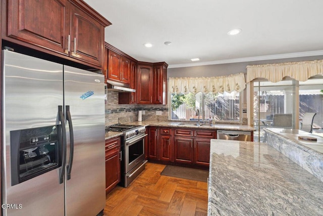 kitchen with appliances with stainless steel finishes, a sink, light stone countertops, dark brown cabinets, and backsplash