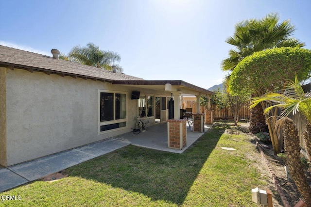 back of house featuring a lawn, a patio area, fence, and stucco siding