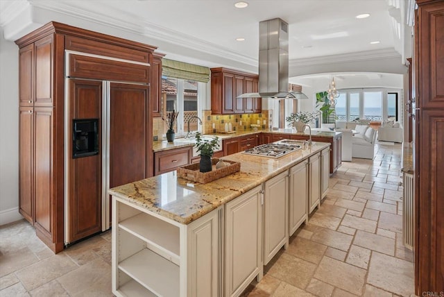 kitchen featuring paneled built in refrigerator, island exhaust hood, crown molding, stone tile flooring, and stainless steel gas stovetop