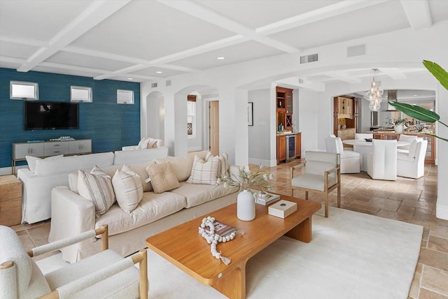 living area featuring arched walkways, stone tile flooring, visible vents, an accent wall, and coffered ceiling