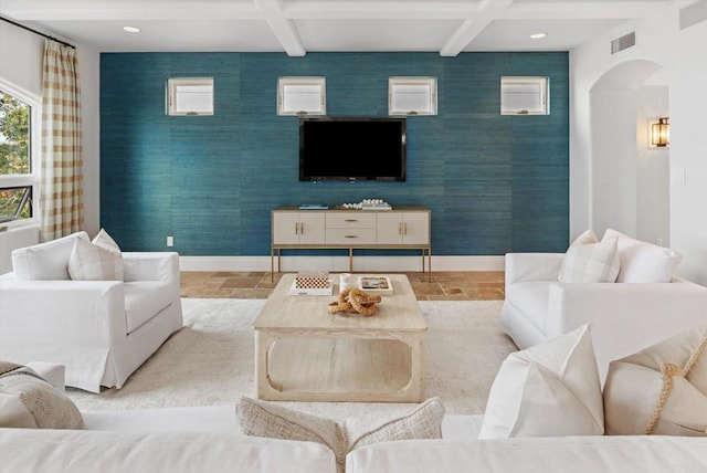 living room featuring wallpapered walls, stone tile floors, visible vents, arched walkways, and baseboards