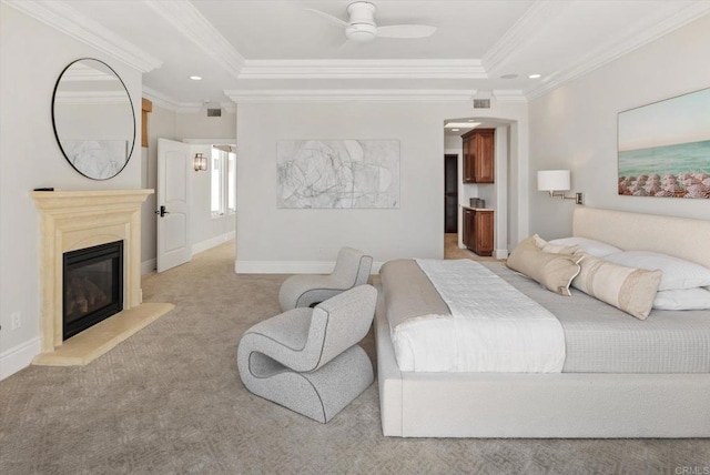 bedroom with light carpet, a tray ceiling, a glass covered fireplace, and baseboards