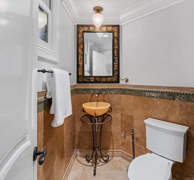 bathroom with tile walls, toilet, a wainscoted wall, crown molding, and a sink