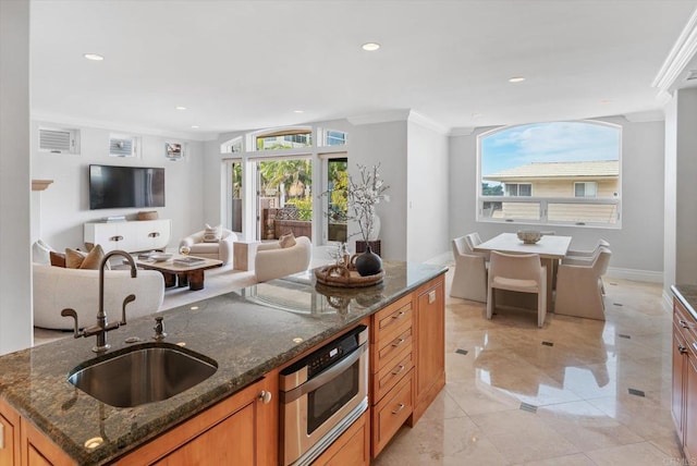 kitchen with recessed lighting, ornamental molding, open floor plan, a sink, and dark stone countertops