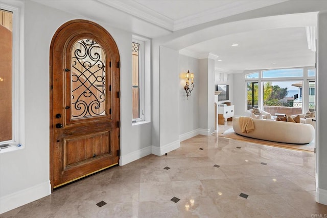 entrance foyer with baseboards, ornamental molding, and arched walkways