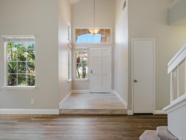 entrance foyer featuring visible vents, baseboards, a towering ceiling, stairway, and wood finished floors