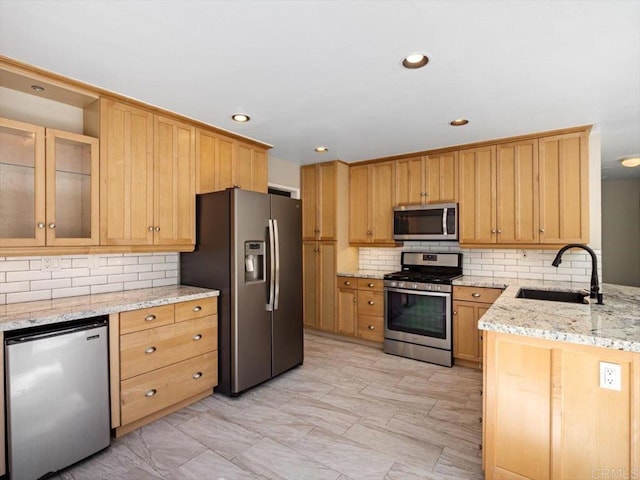 kitchen with stainless steel appliances, backsplash, glass insert cabinets, a sink, and light stone countertops