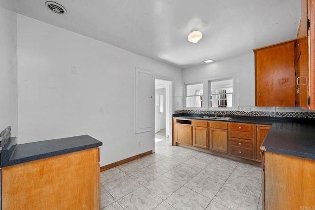 kitchen with a sink, visible vents, brown cabinets, decorative backsplash, and dark countertops