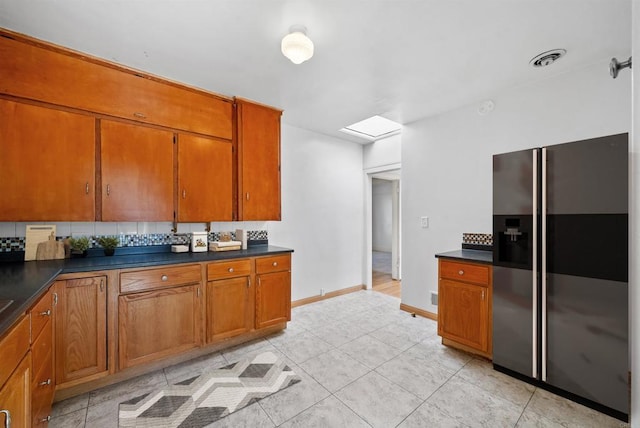 kitchen featuring brown cabinets, dark countertops, visible vents, decorative backsplash, and stainless steel fridge with ice dispenser