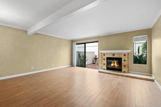 unfurnished living room with crown molding, baseboards, beamed ceiling, a tile fireplace, and wood finished floors