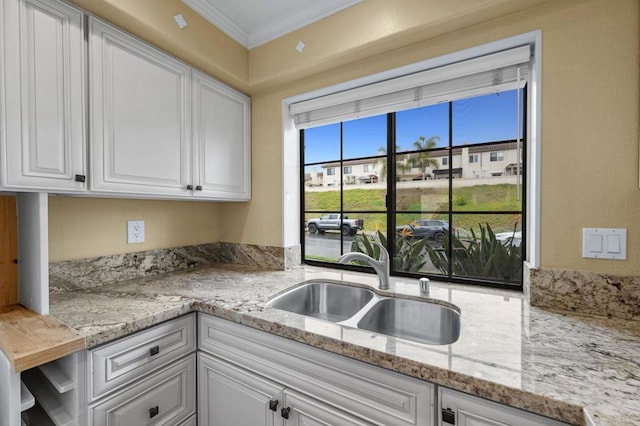 kitchen with white cabinetry, ornamental molding, light stone countertops, and a sink