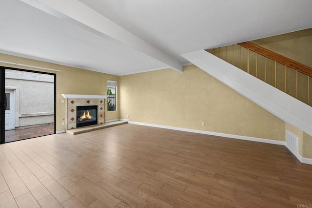 unfurnished living room featuring beam ceiling, a tile fireplace, baseboards, and wood finished floors