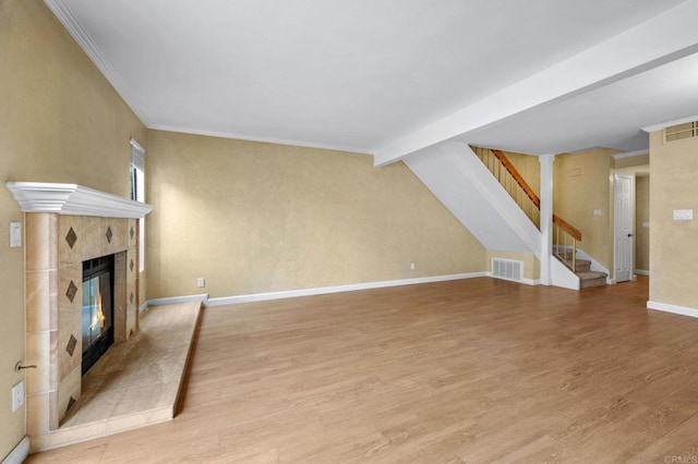 unfurnished living room with light wood finished floors, visible vents, baseboards, a tiled fireplace, and stairs