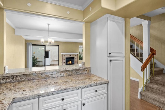 kitchen featuring light stone counters, wood finished floors, ornamental molding, white cabinets, and a glass covered fireplace