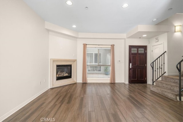 unfurnished living room with a glass covered fireplace, wood finished floors, recessed lighting, and stairs