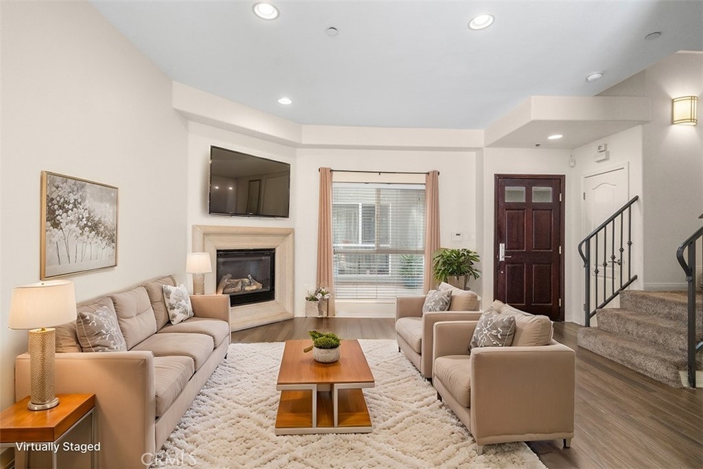 living room with stairs, a glass covered fireplace, wood finished floors, and recessed lighting