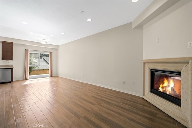 unfurnished living room with a glass covered fireplace, recessed lighting, wood finished floors, and baseboards