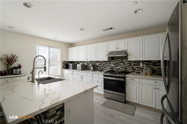 kitchen with under cabinet range hood, a sink, white cabinets, appliances with stainless steel finishes, and backsplash