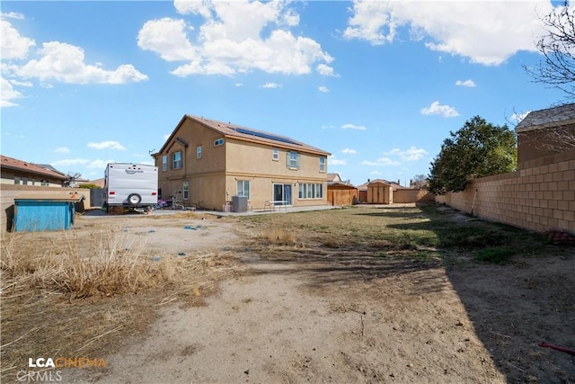 back of house with stucco siding, a fenced backyard, and solar panels