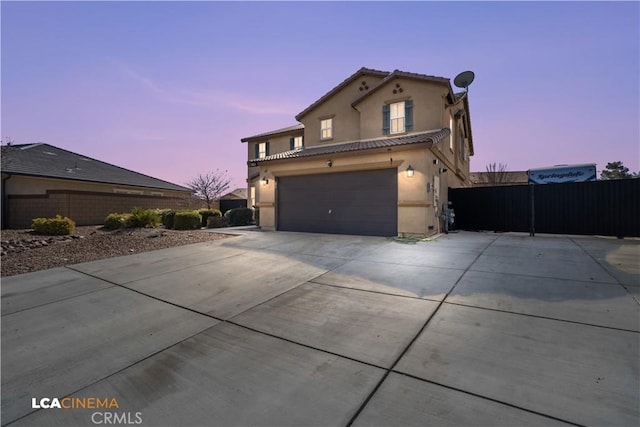 view of front facade with a garage, concrete driveway, a tiled roof, fence, and stucco siding