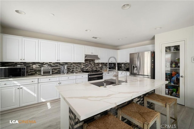 kitchen with tasteful backsplash, white cabinets, stainless steel appliances, under cabinet range hood, and a sink