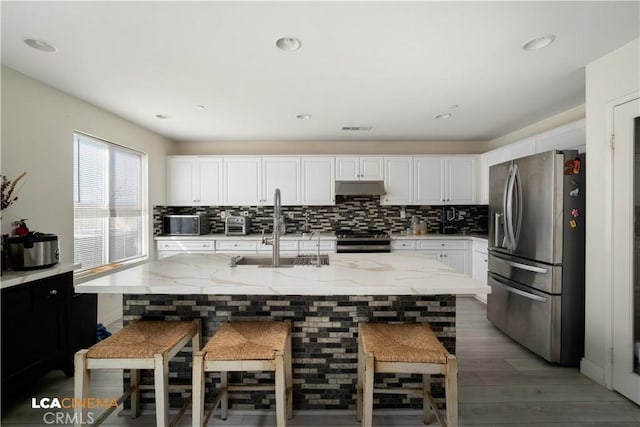 kitchen featuring tasteful backsplash, appliances with stainless steel finishes, white cabinetry, a sink, and under cabinet range hood