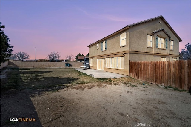 property exterior at dusk featuring a patio area, fence, and stucco siding