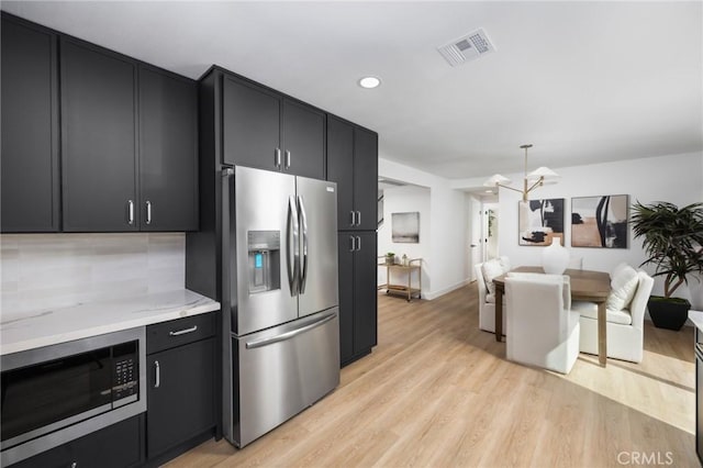 kitchen with light wood finished floors, visible vents, appliances with stainless steel finishes, light stone countertops, and dark cabinets