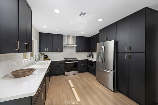 kitchen featuring visible vents, light wood-style flooring, appliances with stainless steel finishes, a sink, and wall chimney range hood