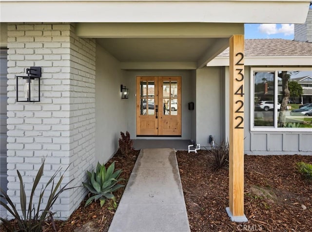 property entrance featuring french doors, brick siding, and roof with shingles