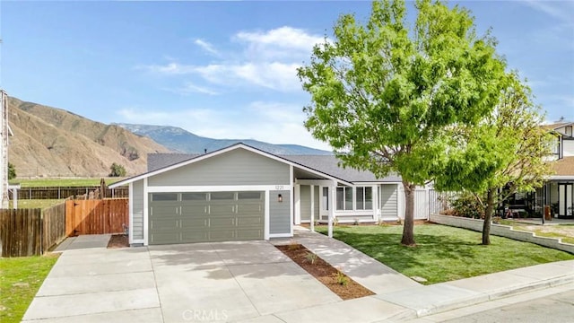 ranch-style house with a garage, concrete driveway, fence, a mountain view, and a front lawn