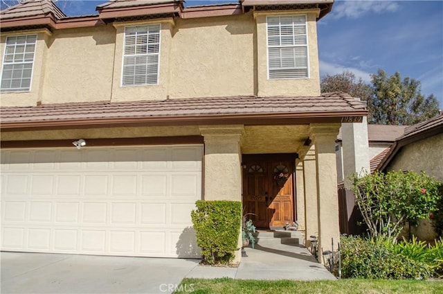 view of front of property with concrete driveway, a tiled roof, an attached garage, and stucco siding