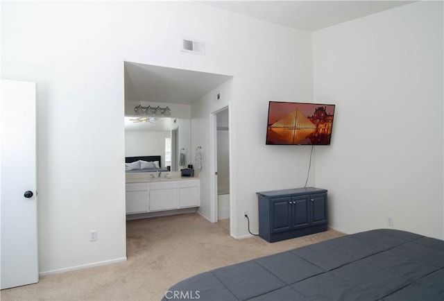 bedroom with baseboards, visible vents, light colored carpet, ensuite bath, and a sink