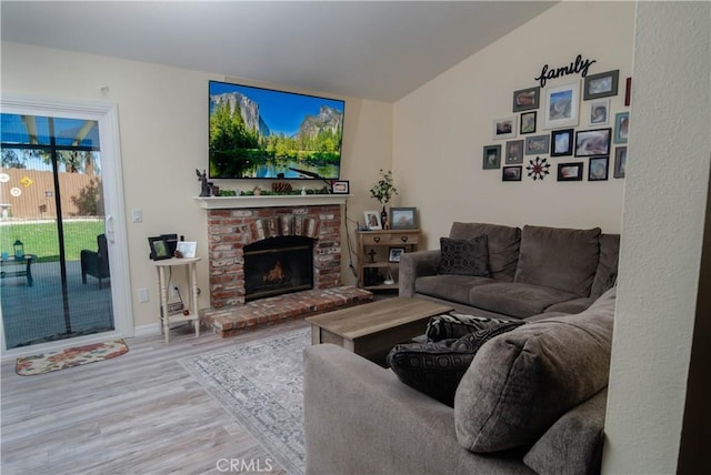 living room featuring vaulted ceiling, a brick fireplace, and wood finished floors