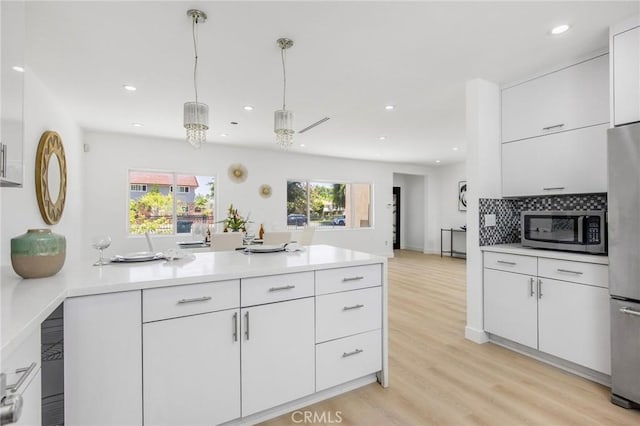 kitchen featuring stainless steel appliances, light countertops, backsplash, white cabinetry, and light wood-type flooring