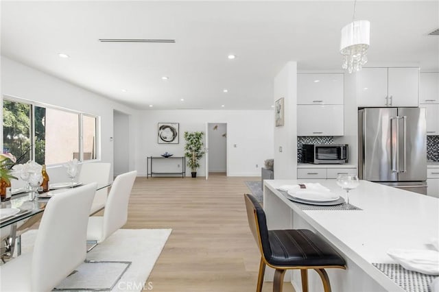 kitchen featuring stainless steel appliances, hanging light fixtures, backsplash, white cabinetry, and light wood-type flooring