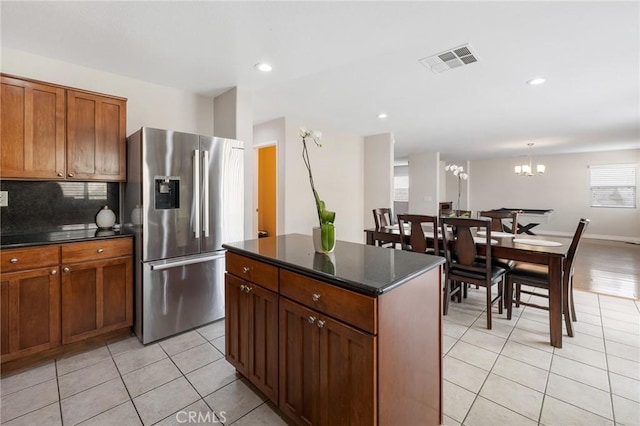 kitchen featuring light tile patterned floors, a kitchen island, visible vents, decorative backsplash, and stainless steel fridge