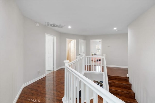 corridor with recessed lighting, wood finished floors, visible vents, baseboards, and an upstairs landing