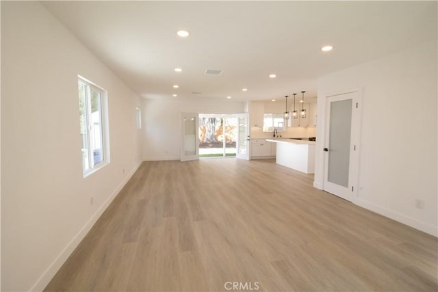 unfurnished living room featuring light wood-type flooring, a sink, baseboards, and recessed lighting