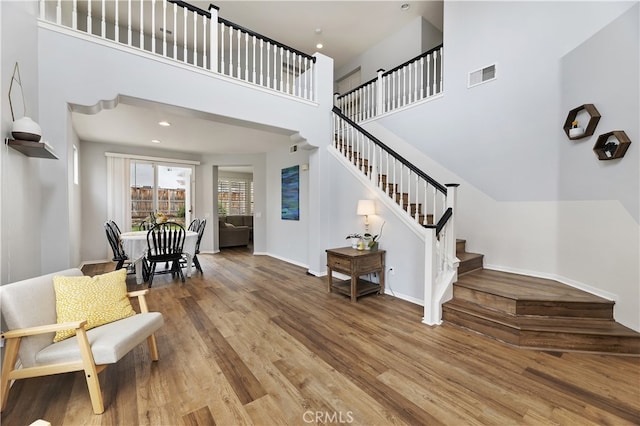 interior space with visible vents, wood finished floors, stairway, baseboards, and a towering ceiling